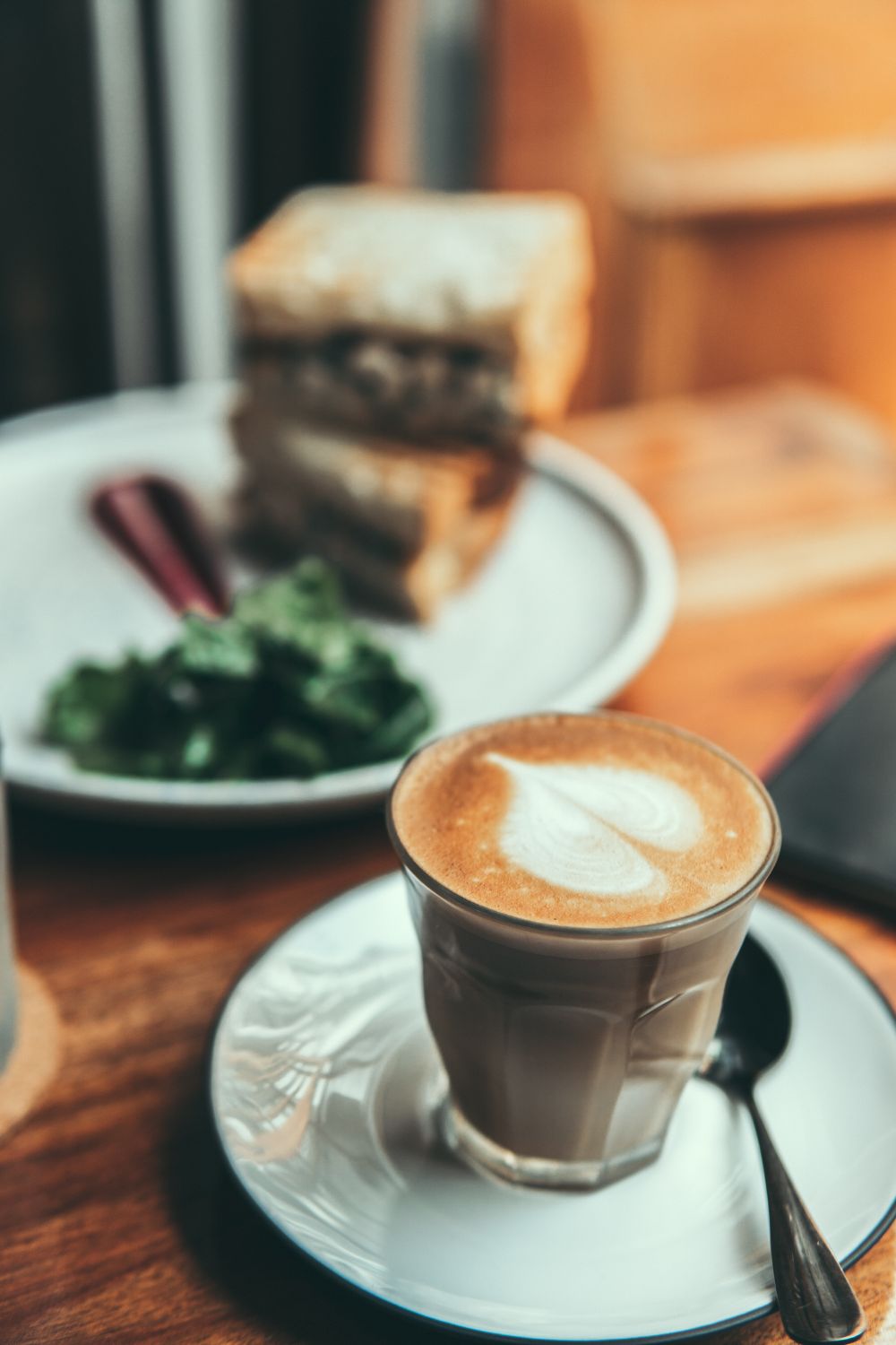 A glass latte with detailed foam art beside brunch